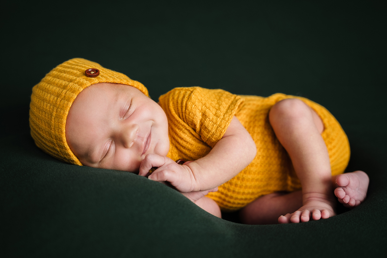 Schlafendes Baby in gelbem Strampler auf grünem Hintergrund – Babyfotograf Vallendar